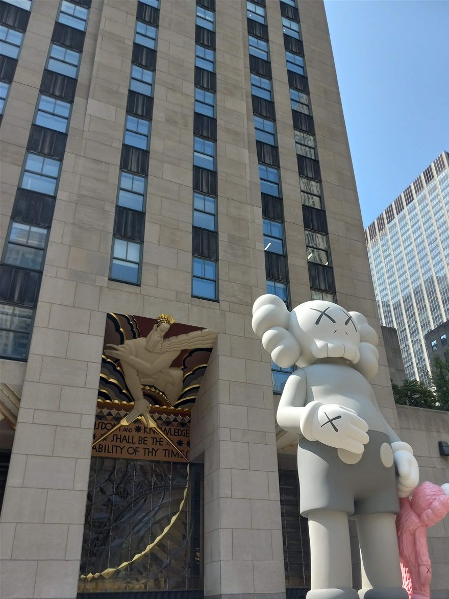 Walking past 30 Rockefeller Center with a KAWS sculpture and a quote from the Bible; 